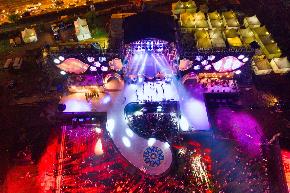 Vista aérea nocturna de un escenario de festival con público congregado