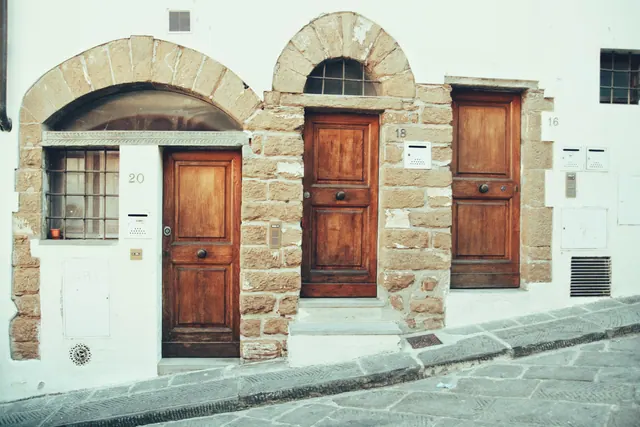 Tres puertas de madera con arcos de piedra en una fachada antigua junto a una calle empedrada