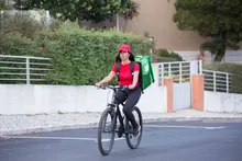 Repartidor con mochila térmica de reparto a la espalda, apoyado en su bicicleta en una calle