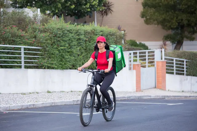 Repartidor con mochila térmica de reparto a la espalda, apoyado en su bicicleta en una calle