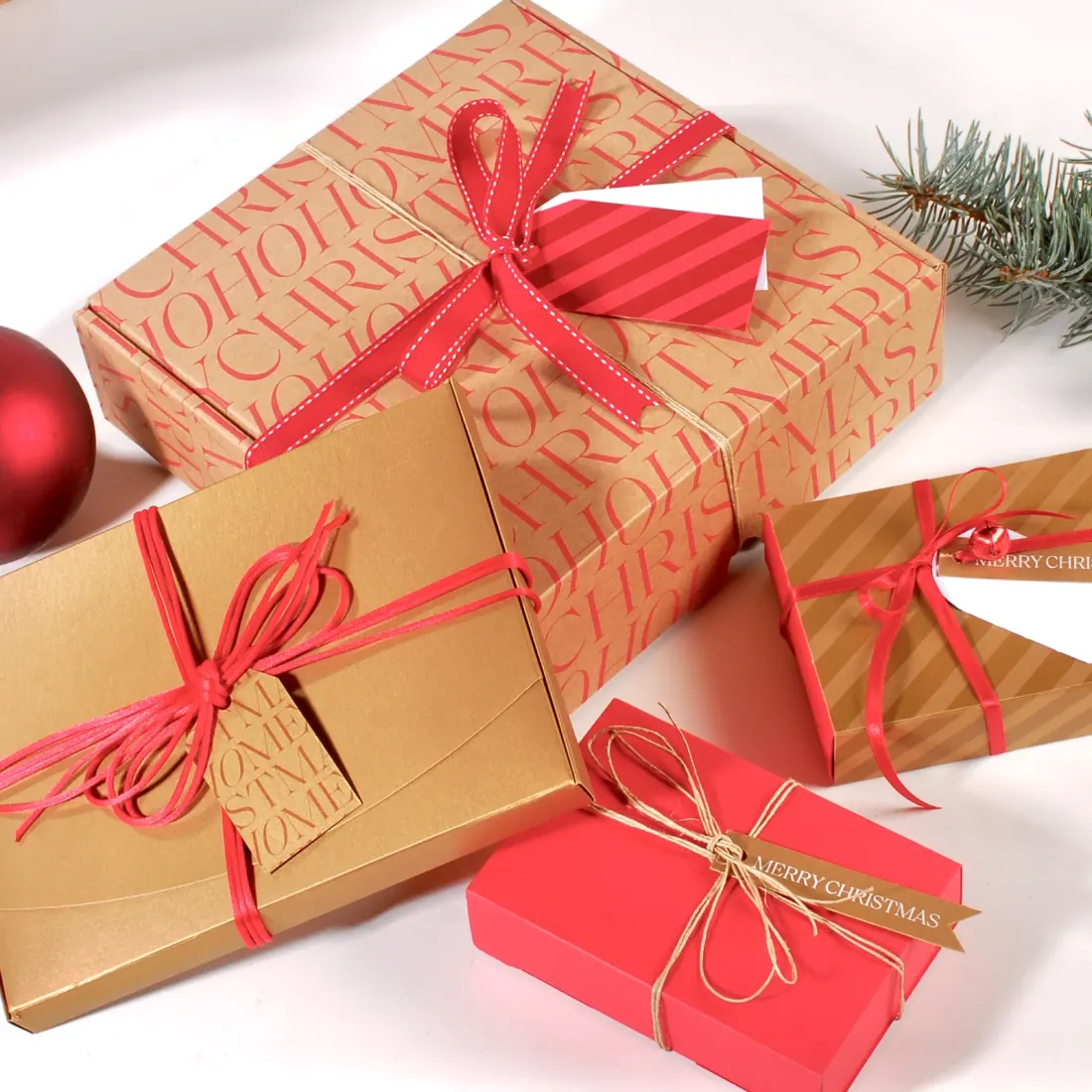 Regalos navideños envueltos con lazos rojos junto a una rama de abeto