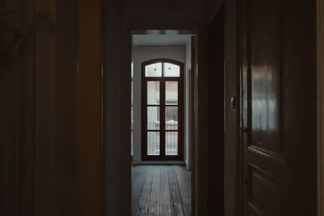 Pasillo en penumbra que da a una habitación con balcón