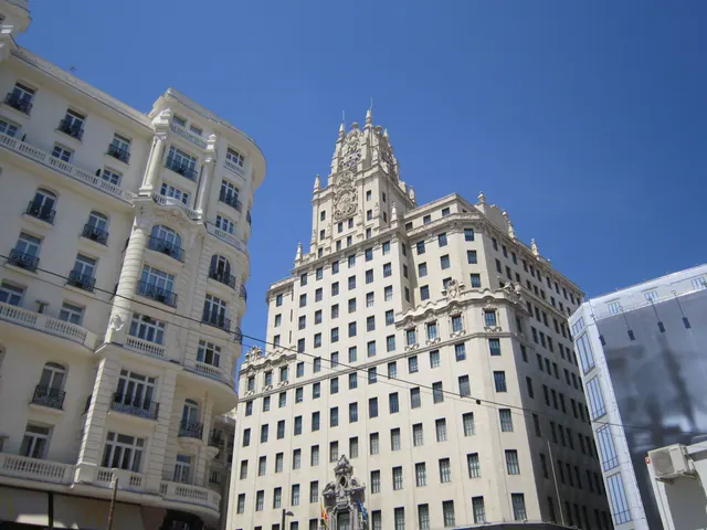 Fachada de un edificio señorial de piedra con grandes ventanales en una avenida urbana