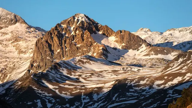 Senderista recorriendo un sendero de alta montaña en los Pirineos con picos nevados al fondo
