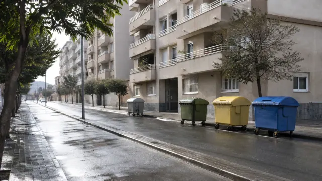 Contenedores de reciclaje de distintos colores en una calle residencial mojada