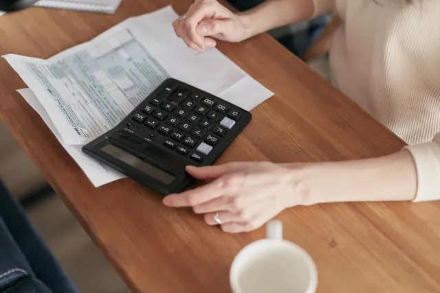 Manos usando una calculadora junto a documentos sobre una mesa