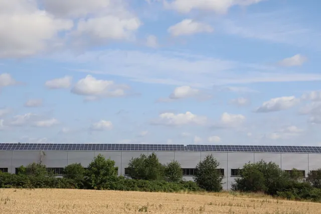 Nave industrial con paneles solares en el tejado junto a un campo