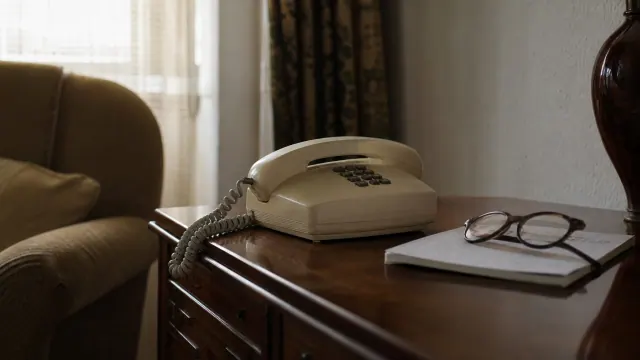 Teléfono de línea fija sobre una mesita junto a gafas y un cuaderno