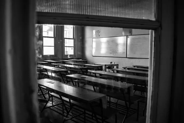 Aula escolar vacía con pupitres y ventanas con persianas