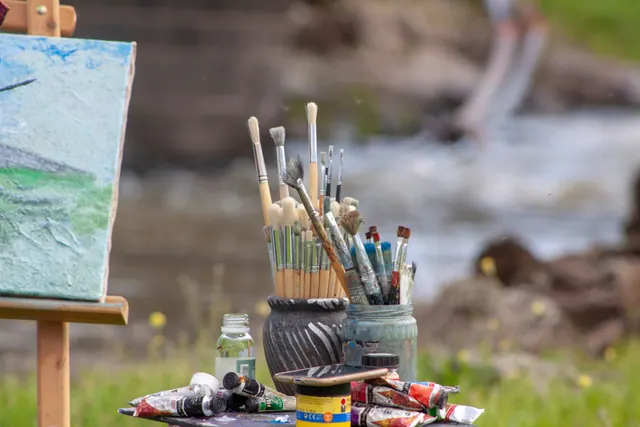 Pinceles y tubos de pintura junto a un caballete al aire libre