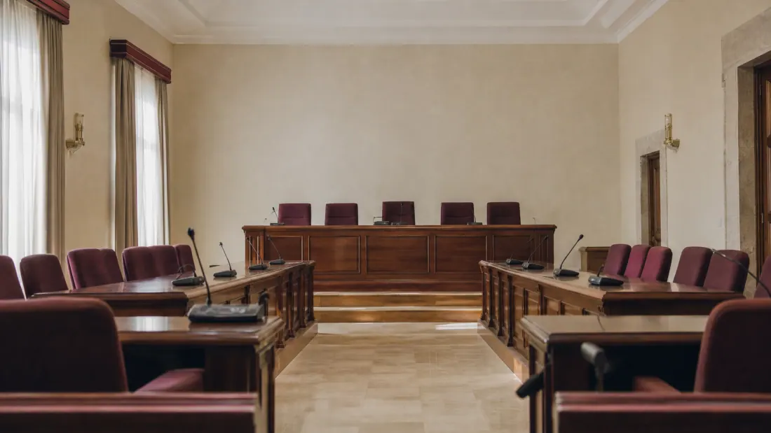 Sala de juicios con estrado de madera y sillas tapizadas en borgoña a ambos lados