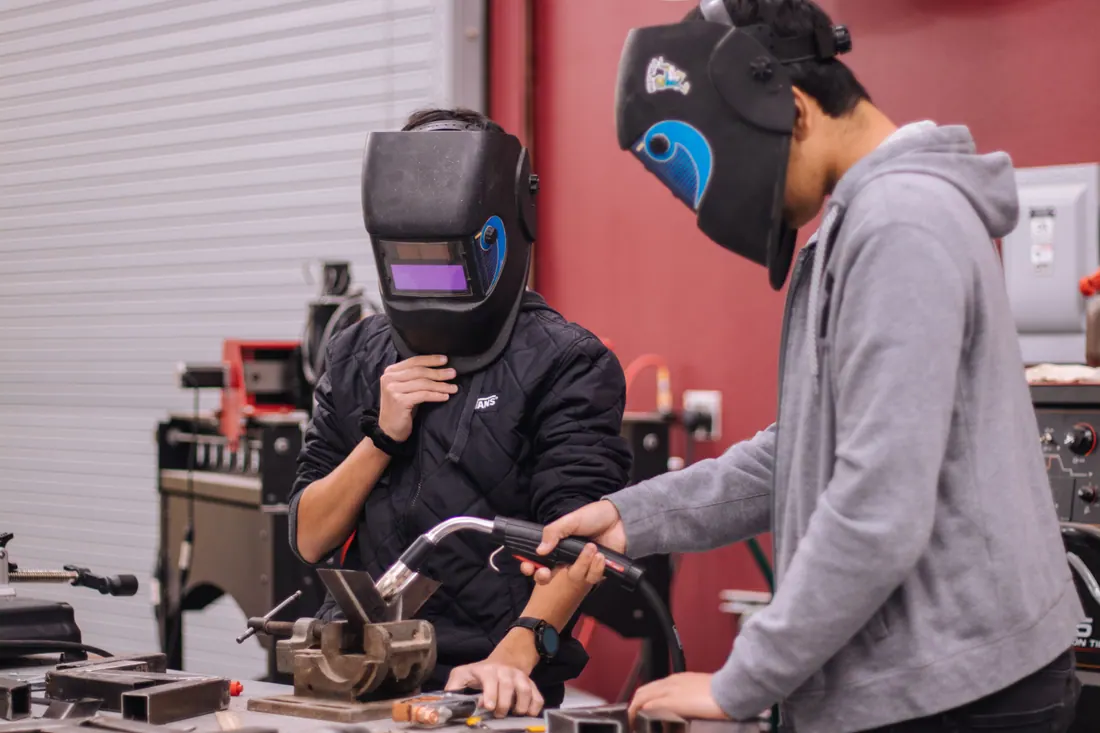 Dos personas con máscaras de soldar practicando en un taller