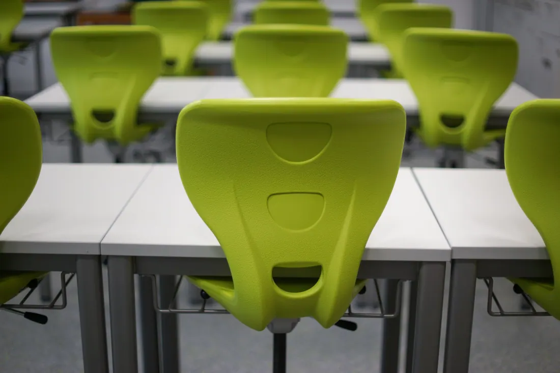 Sillas verdes y mesas blancas en un aula vacía