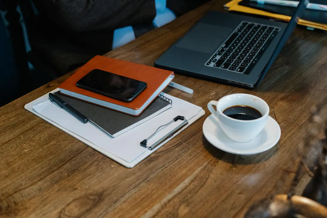 Cuadernos, teléfono, portátil y una taza de café sobre una mesa de madera