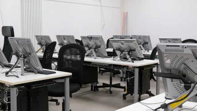 Aula informática vacía con varios monitores y sillas de oficina