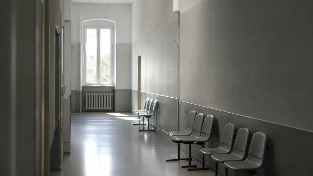 Pasillo de hospital con sillas de espera y puerta de entrada al fondo