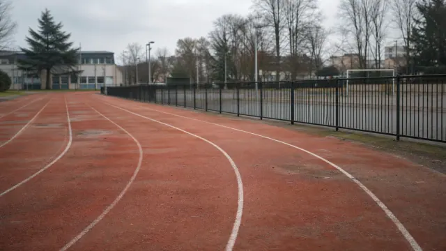 Pista de atletismo de arcilla roja con líneas de carril blancas y valla metálica