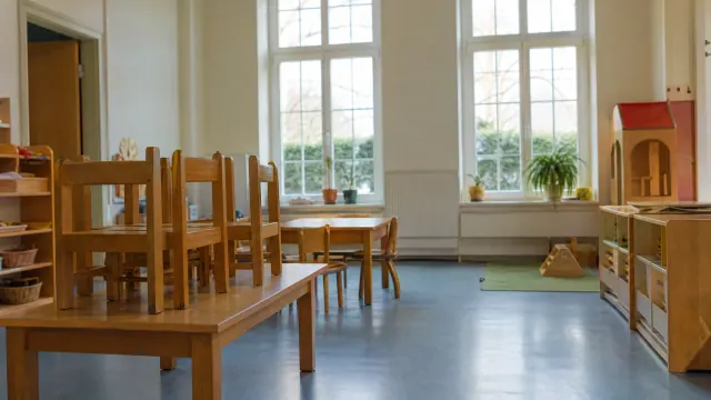 Aula de educación infantil con mesas y sillas de madera, muebles de almacenaje