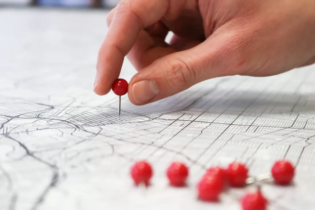 Una mano coloca una chincheta roja sobre un mapa de calles