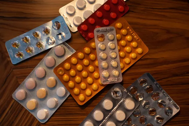 Varios blísteres de pastillas de distintos colores sobre una mesa de madera