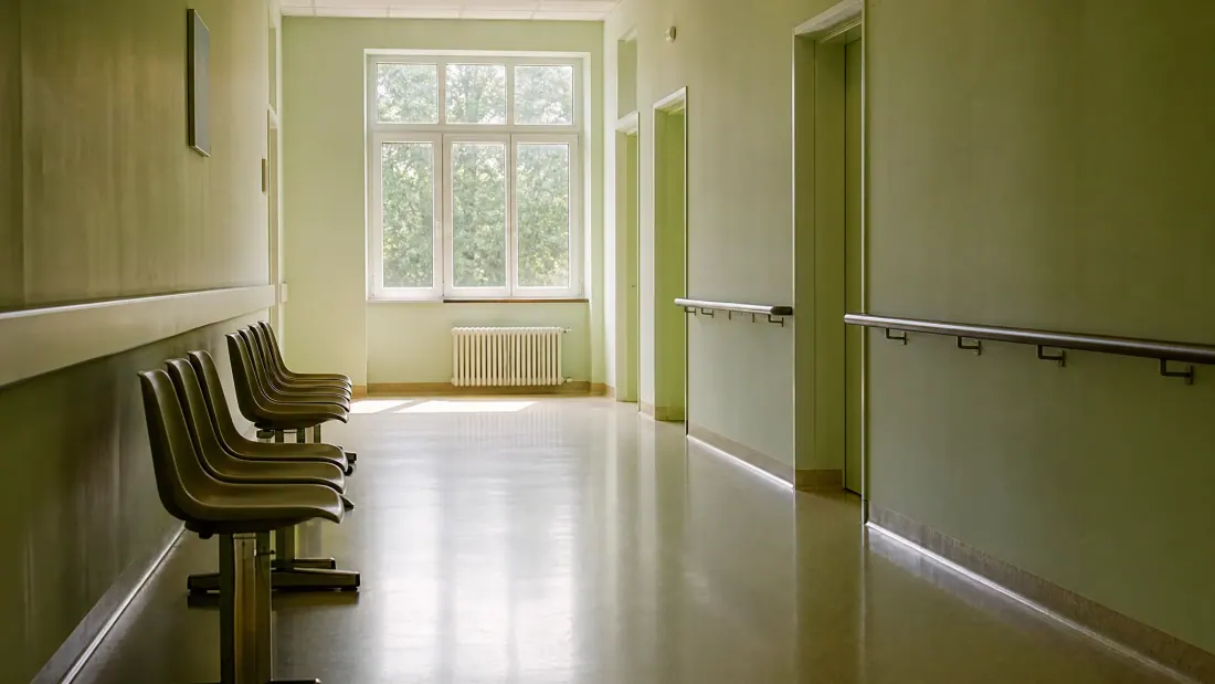 Pasillo de centro sanitario con sillas de espera junto a una ventana