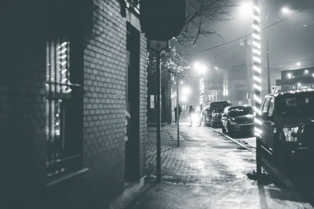 Calle nocturna con niebla, coches aparcados y farolas encendidas