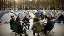 Un grupo de personas acampadas en una plaza urbana rodeadas de tiendas de campaña