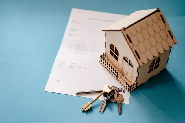 Una casa de madera en miniatura con llaves sobre un documento