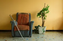 Un sillón viejo con una muleta junto a una planta artificial