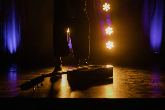 Guitarra sobre un escenario iluminado con luces moradas y doradas