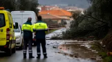 Dos operarios de emergencias junto a vehículos en una carretera inundada con ramas