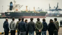 Grupo de personas de espaldas observando un buque carguero en puerto