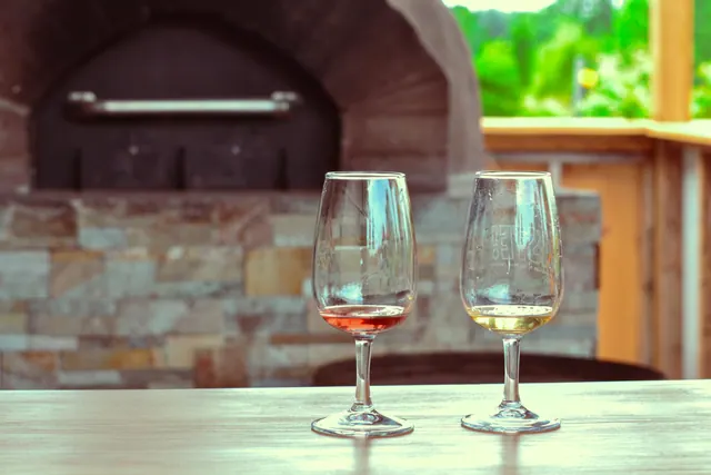 Dos copas de vino sobre una mesa junto a un horno de piedra