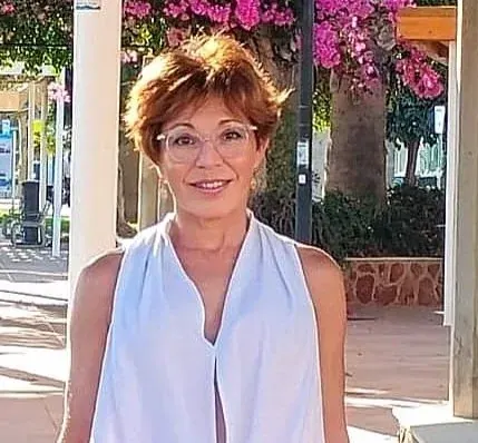 Una mujer con gafas sonríe bajo un porche con buganvillas en flor