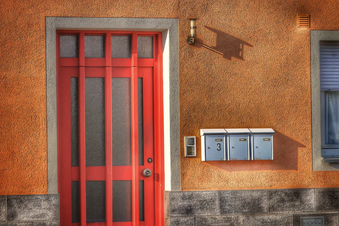 Fachada con puerta roja, buzones y portero automático