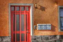 Fachada con puerta roja, buzones y portero automático