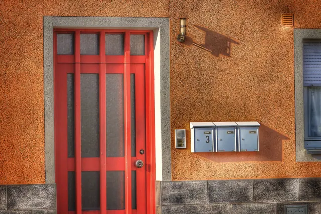 Fachada con puerta roja, buzones y portero automático