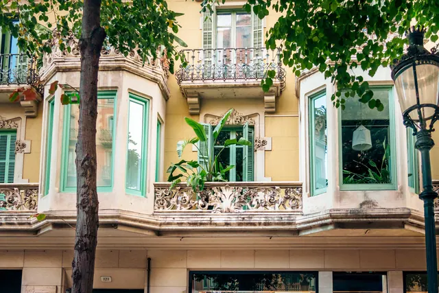 Fachada modernista con balcones y plantas en una calle urbana