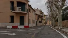 Calle de un pueblo medieval italiano con edificios de fachada ocre y bolardos rojos