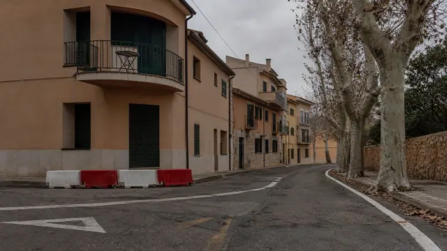Calle de un pueblo medieval italiano con edificios de fachada ocre y bolardos rojos