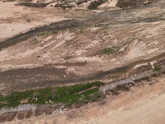 Vista aérea de un cauce seco con escombros y vegetación dispersa