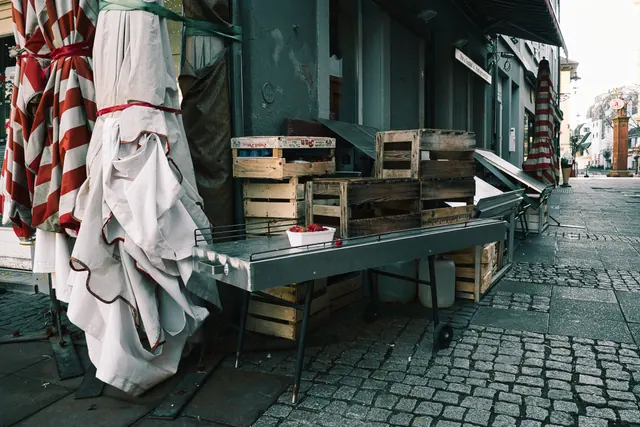 Cajas de madera y sombrillas plegadas frente a un comercio en una plaza