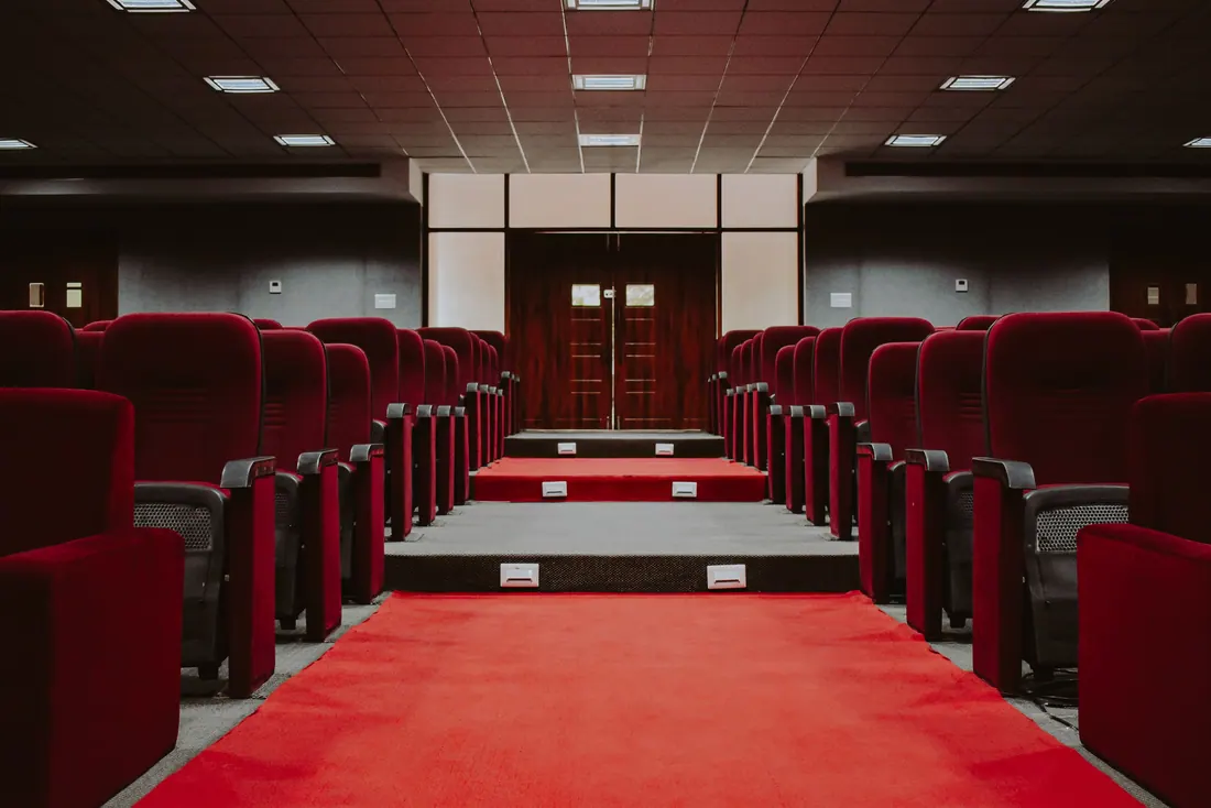 Interior de un auditorio vacío con butacas rojas y pasillo central