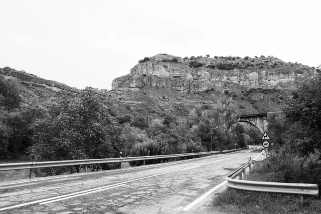 Carretera secundaria de montaña con quitamiedos metálico al borde de un desnivel rodeado de vegetación