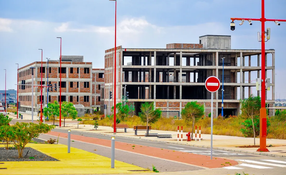 Acera y calzada recién urbanizadas junto a un solar sin edificar con árboles jóvenes plantados