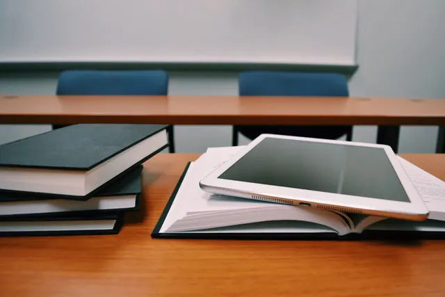 Libros y una tableta sobre un pupitre en un aula