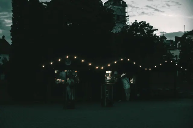 Puestos de mercado nocturno iluminados con luces frente a una torre