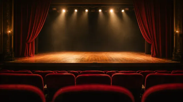 Escena de un teatro con el escenario iluminado y butacas rojas en primer plano