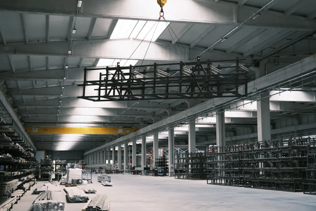 Una nave industrial con una grúa elevando una estructura metálica sobre estanterías de almacenaje