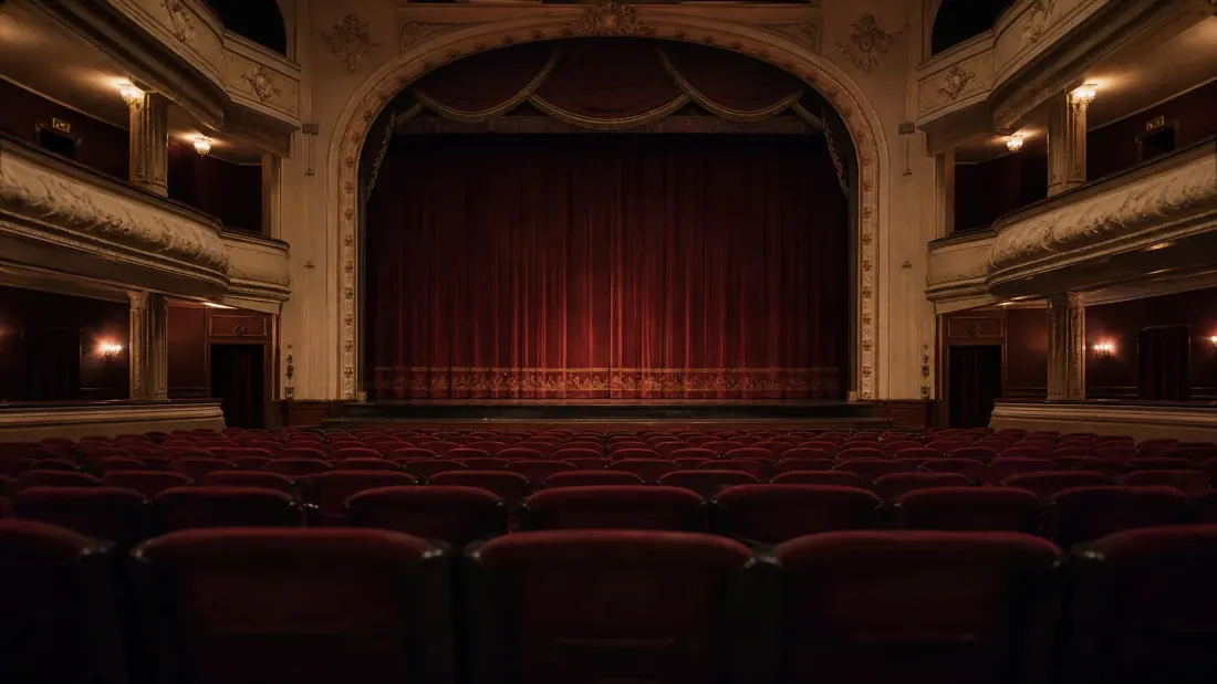 Interior de teatro con butacas rojas y cortina roja cerrada en el escenario
